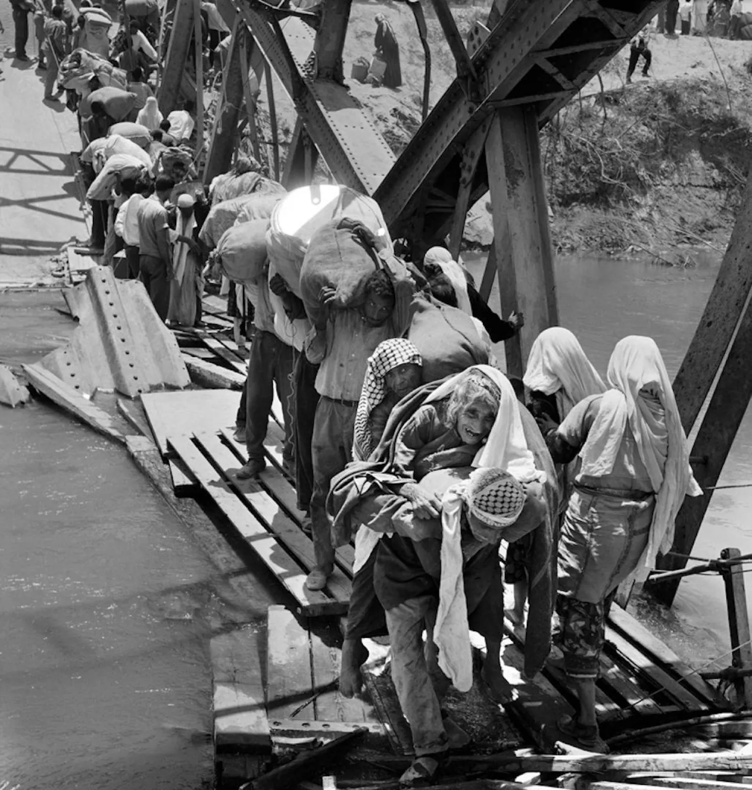 Palestinian refugees carrying bundles climb across the twisted wreckage of the Allenby Bridge