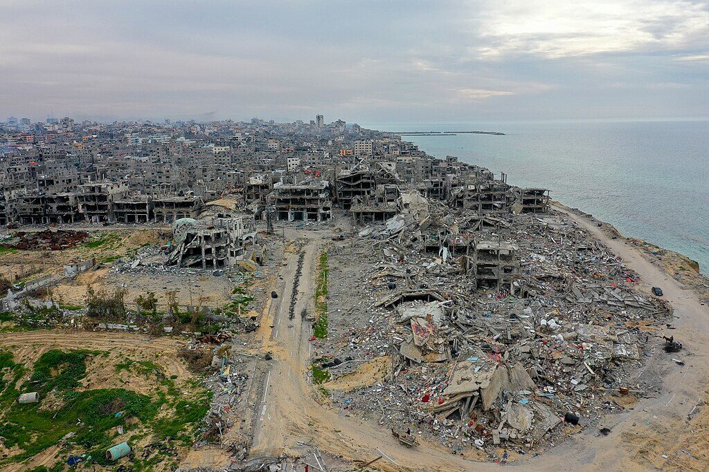 Aerial photograph of the Beach refugee camp in Gaza showing whole blocks of buildings reduced to rubble, with few intact structures remaining.