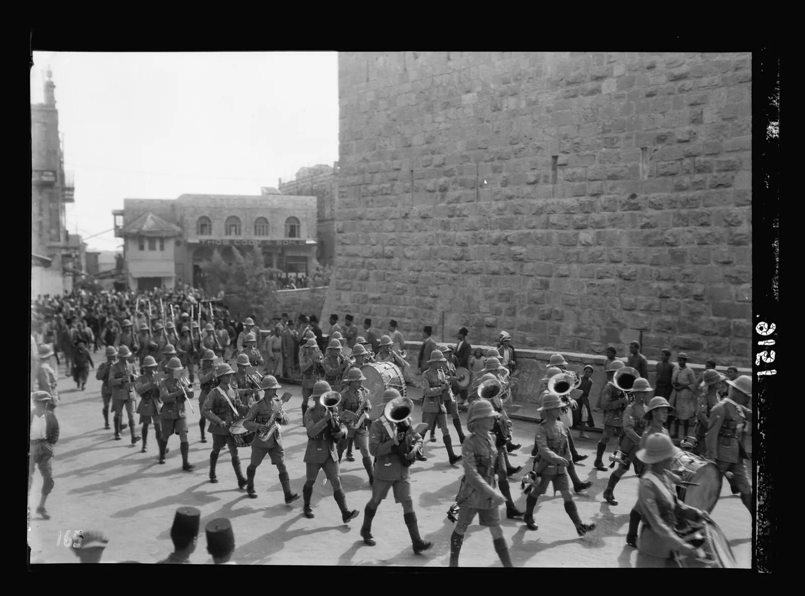 Columns of British soldiers marching through a Jerusalem street beside the Old City wall