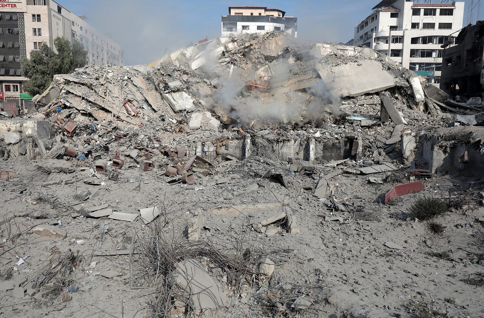 A Gaza apartment block reduced to twisted concrete and rebar, with surrounding buildings showing blast damage.