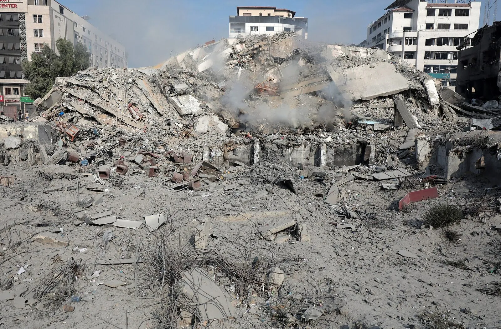 A Gaza apartment block reduced to twisted concrete and rebar, with surrounding buildings showing blast damage.