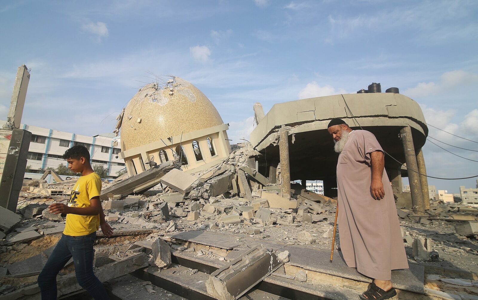 Palestinians standing on a mound of debris beside a destroyed multi-story building in Khan Younis, southern Gaza.