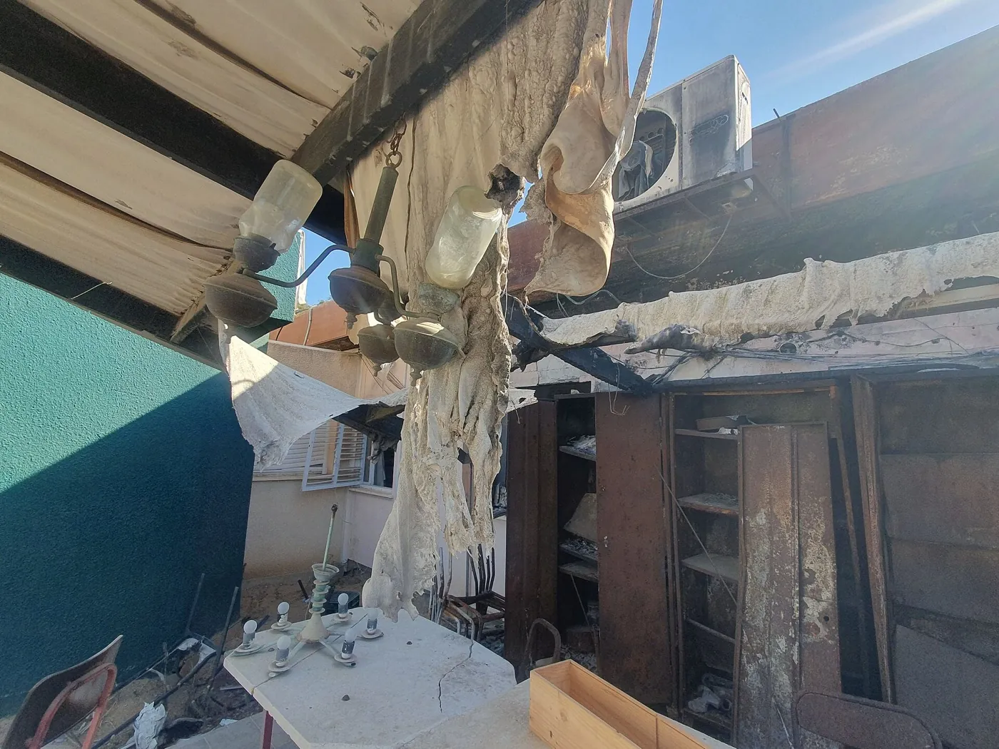 The fire-blackened interior of a home in Nir Oz, with melted light fixtures, charred cabinets, and a burned-through ceiling.