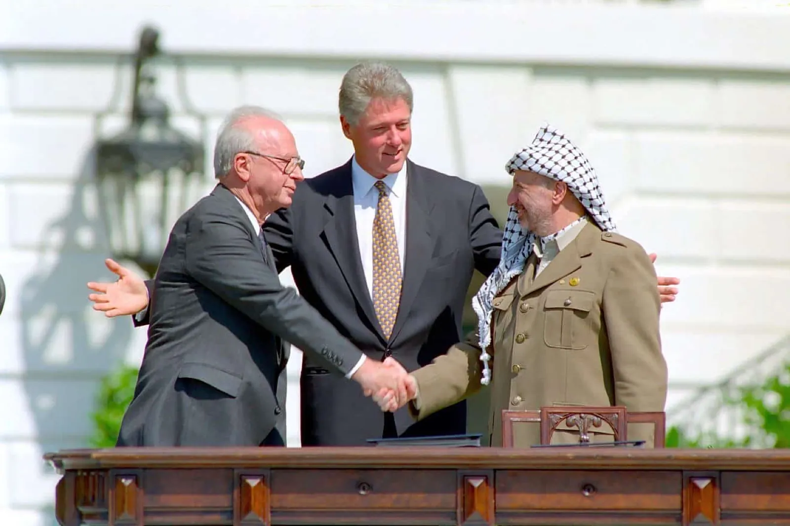 Yitzhak Rabin and Yasser Arafat shake hands as Bill Clinton stands between them on the White House lawn