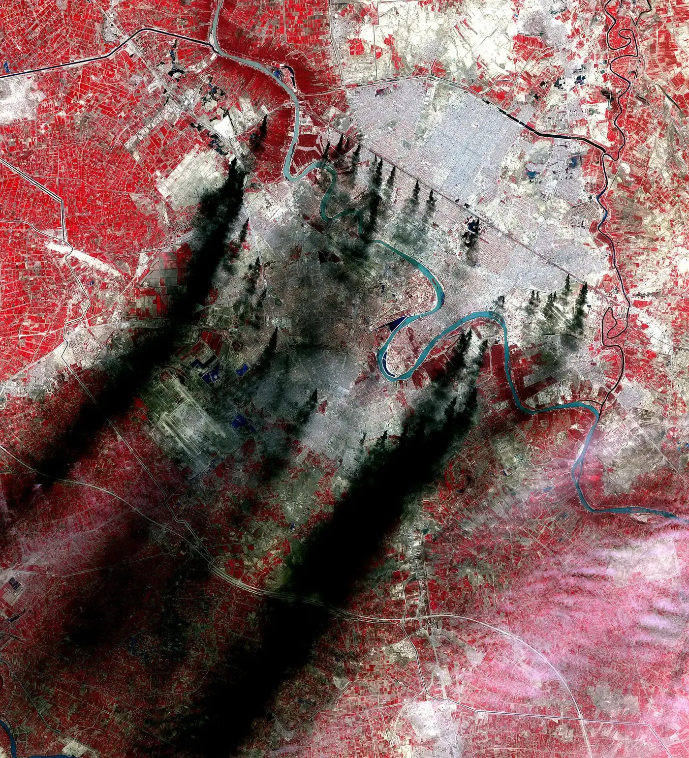 Baghdad seen from orbit on March 31, 2003, eleven days into the invasion, in false color: vegetation shows red and black plumes of burning oil drift across the city.