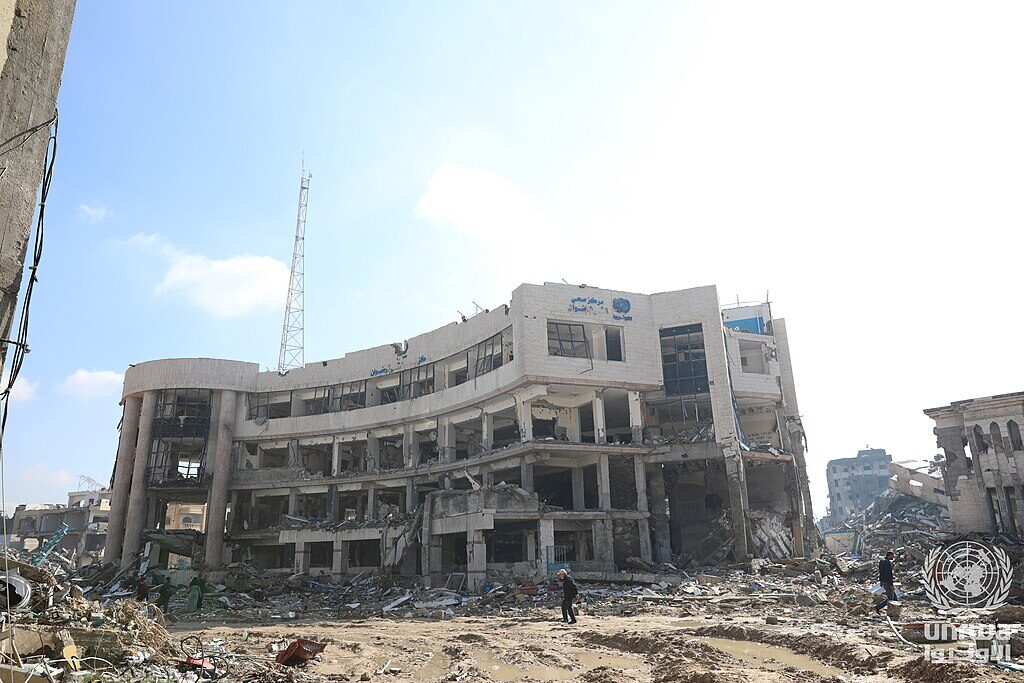 The destroyed UNRWA Sheikh Radwan health center — the building's concrete roof has collapsed onto twisted metal and medical supplies.
